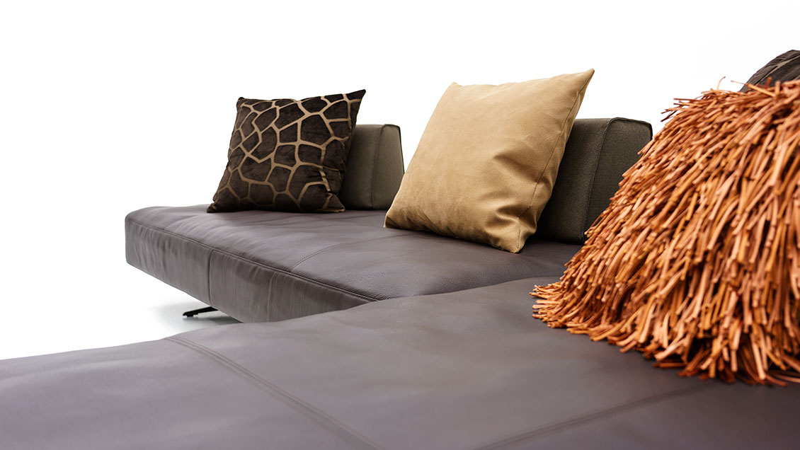 EASY -Detailbild der gewollt weichen Sitzfläche in braunen Leder mit passenden Dekokissen