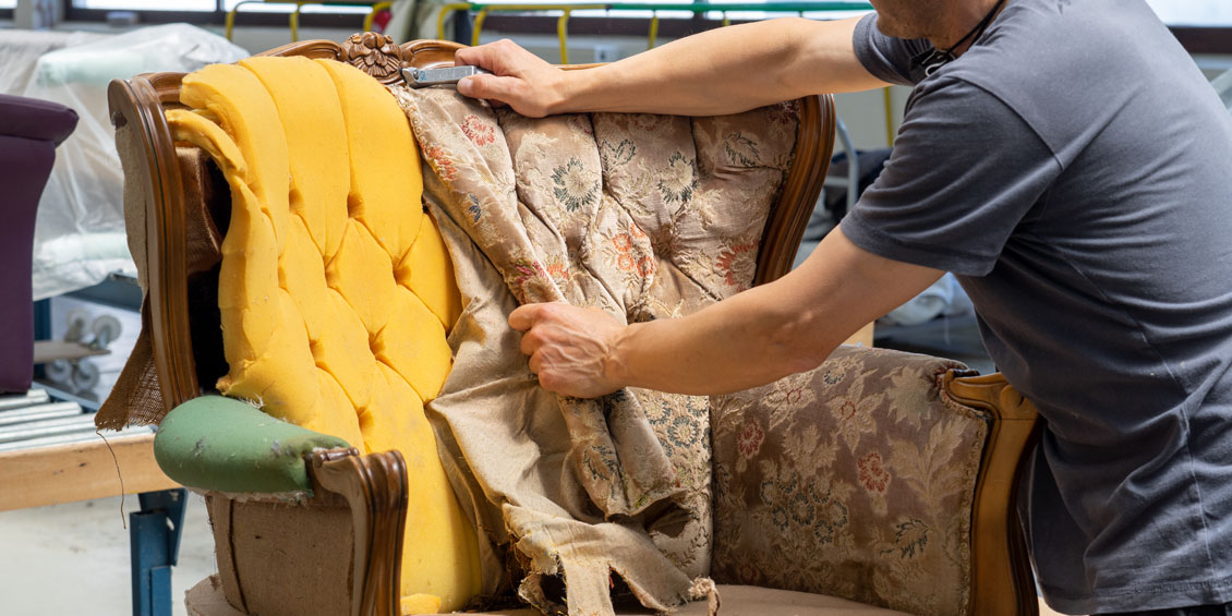 Polsterer takelt alten Bezugsstoff am Chesterfield-Sessel ab
