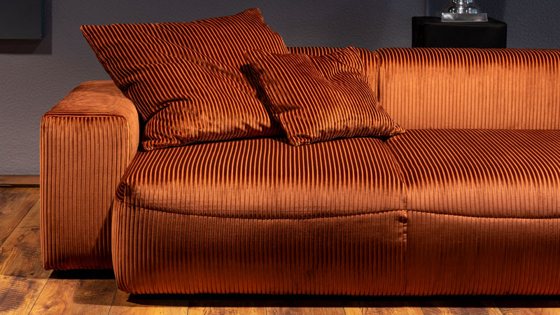 Detailbild vom neuen Lounge-Sofa Carlo mit Zierkissen, bezogen im Cord-Stoff kupfer